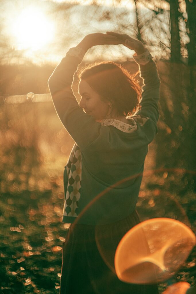 Sustainable Fashion at ilovecarousel.com, inspired by vintage fashion of the past. A female model dances in the evening sun wearing an organic cotton cardigan, a blouse printed with bicycles and a burgundy corduroy skirt. 